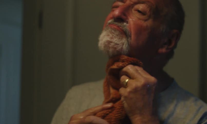 Older man wiping his face with a brown towel in the bathroom then smiling