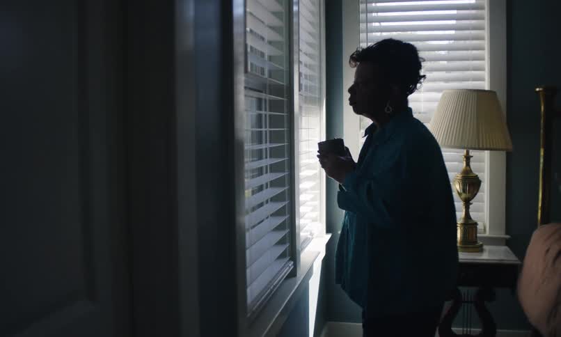 Woman looks nervously out a window drinking from a cup