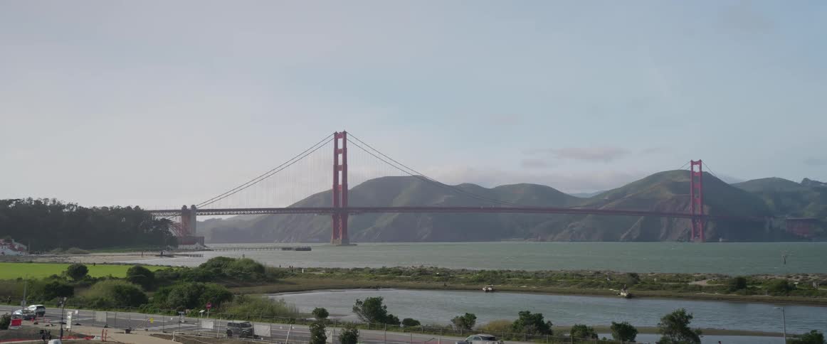 A wide panoramic view showcases san franciscos renowned golden gate bridge majestically extending over the expansive bay linking to the rolling marin headlands set beneath a slightly hazy overcast sky