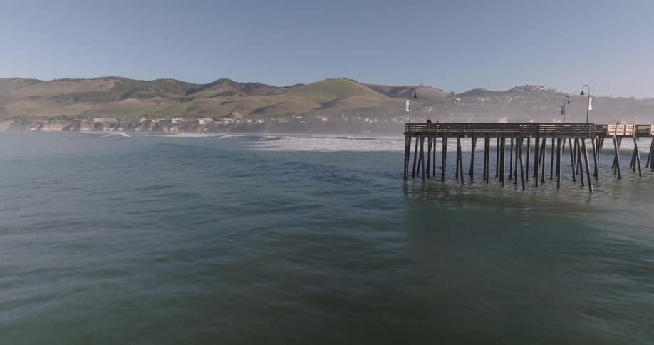 Waves roll past a pier near a town