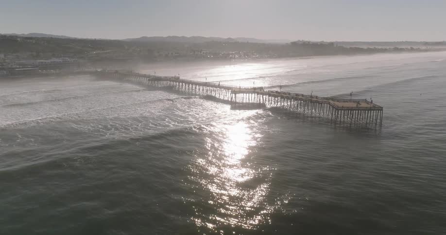 Landscape of a long pier on the beach with a city in the background