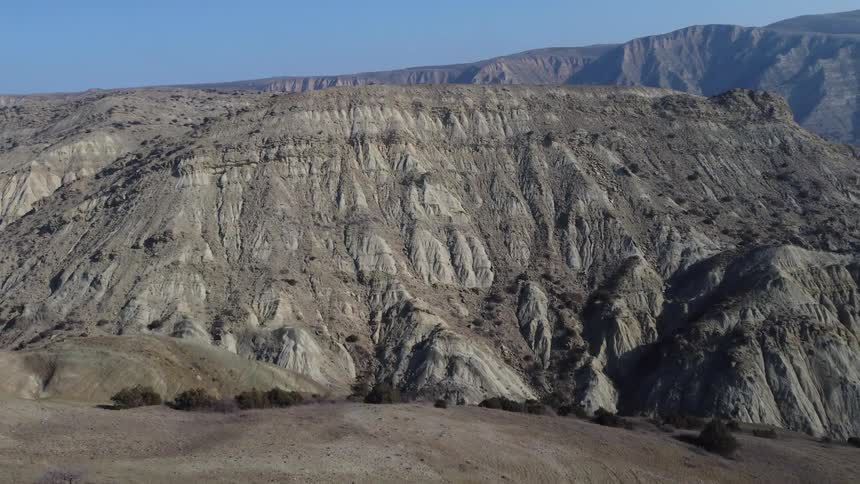 Aerial view shows arid terrain with rock formations and hills in the background