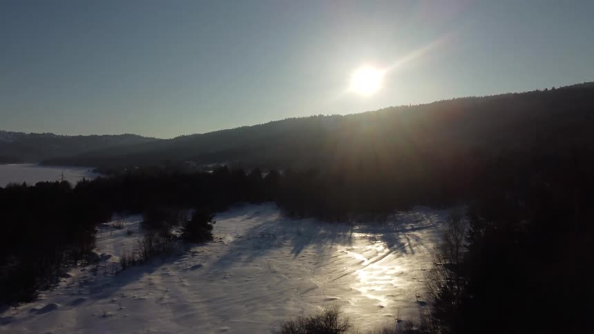 Beginning near ground level the view rises displaying an expansive winter with a snowy expanse under the setting sun