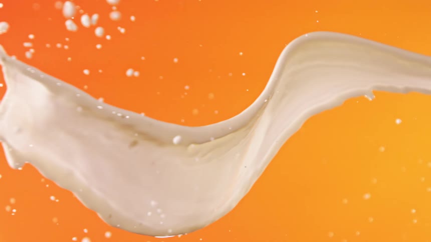 A splash of white liquid is captured against a bright orange background