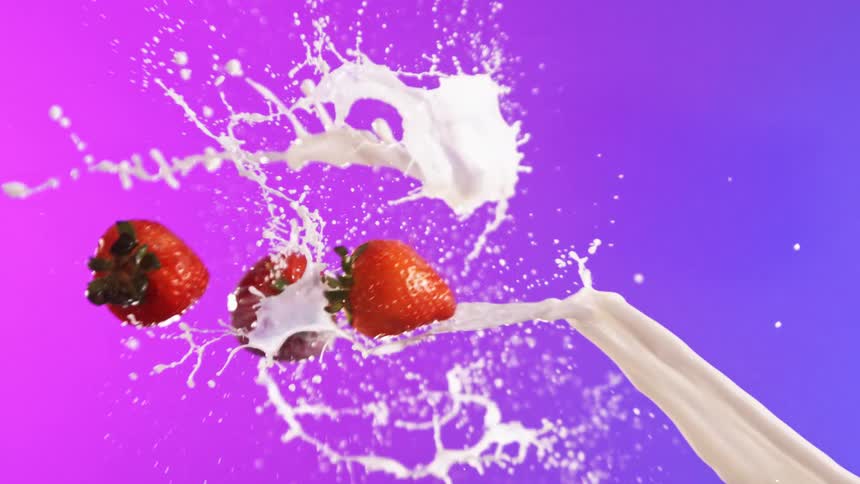 Vivid strawberries launched from the right smash into a powerful stream of stark white dairy arriving from the opposing direction creating an energetic scattering over a seamless purple backdrop