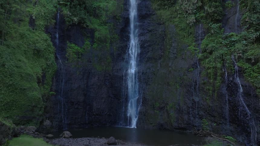 Initially focusing on the middle section of a waterfall the perspective expands to reveal the full cascade down a lush cliffside and the serene pool formed at its base