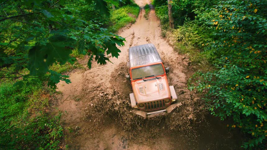 Slow motion aerial view of a jeep driving on a muddy road in the forest