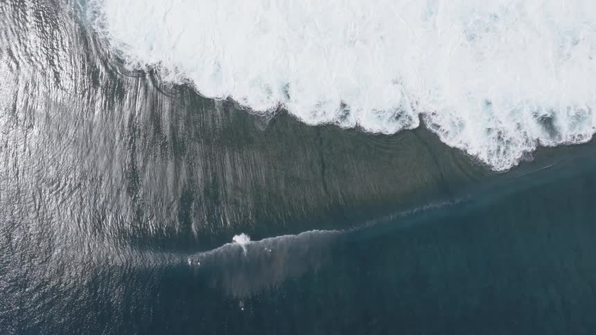 A wave breaking in a dark blue ocean with surfers waiting in the water