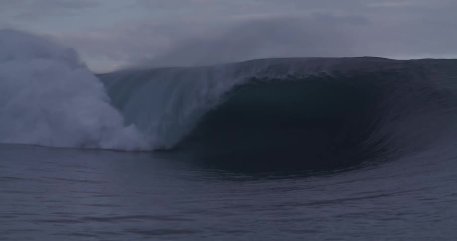 Surfer riding a large breaking wave falls off the surfboard on an overcast day
