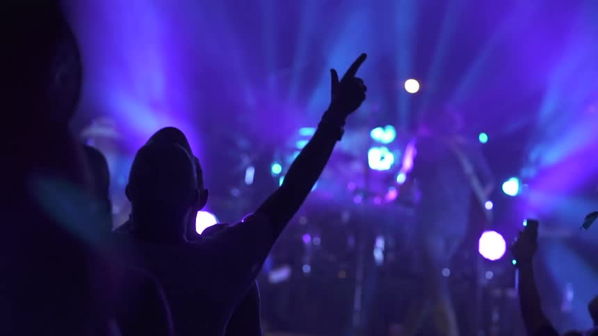A rock band performing on stage as vibrant lights illuminate the background and an enthusiastic audience cheers them on