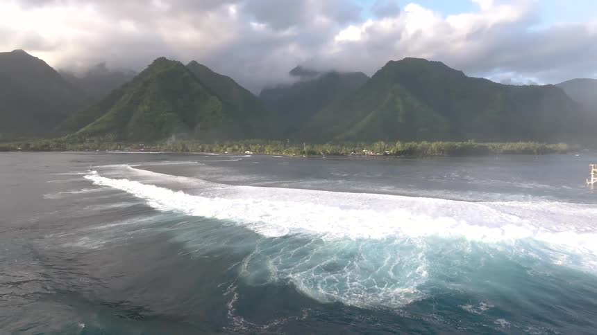 Boats and jetskis out past the breaking foaming waves off the mountains and coast of tahiti