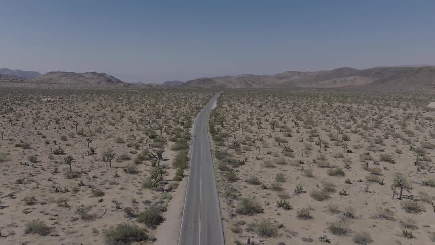 An aerial view of a long straight road stretching across a vast desert landscape with sparse vegetation and distant mountains