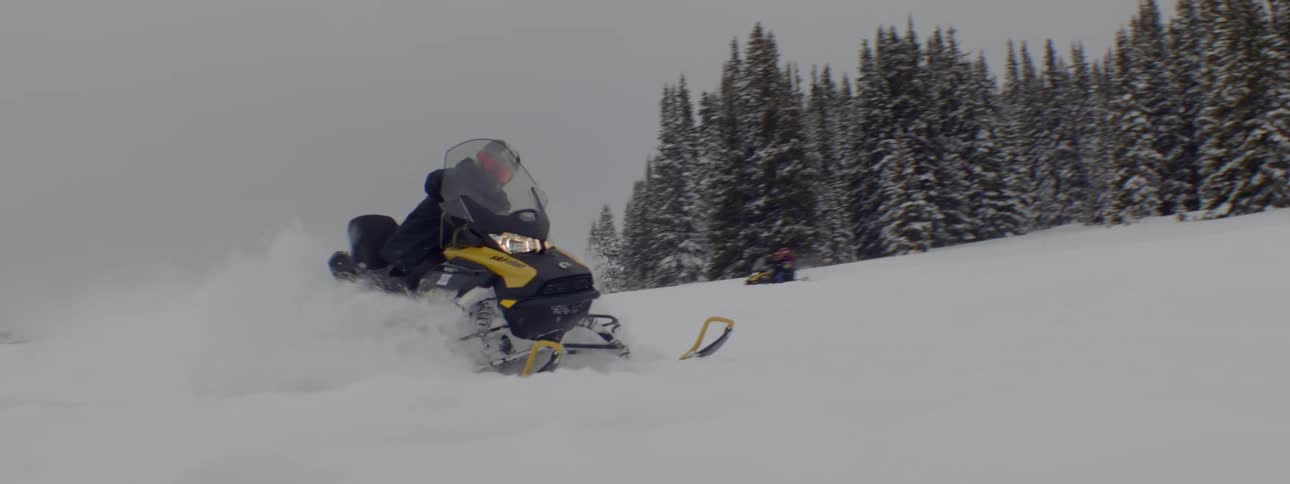 2 people on snowmobile splashing snow passing by