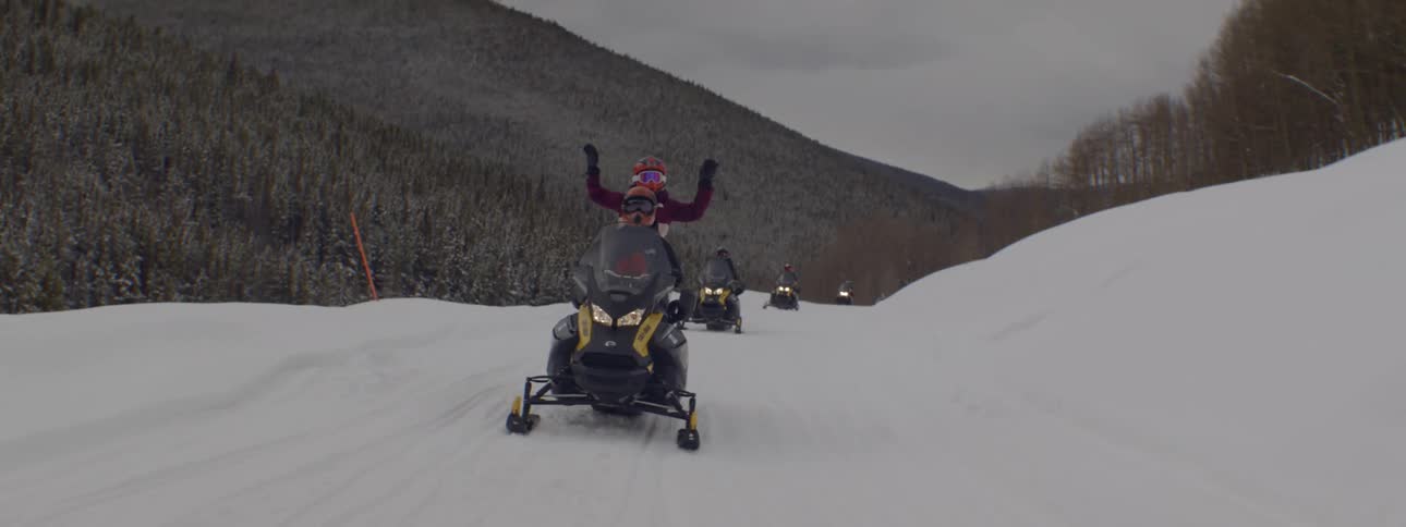 People on snowmobiles through the mountains on a cloudy day