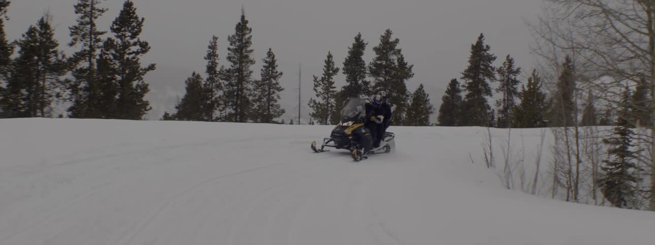 A small group of people are riding snowmobiles on a snowcovered mountain road on a cloudy day