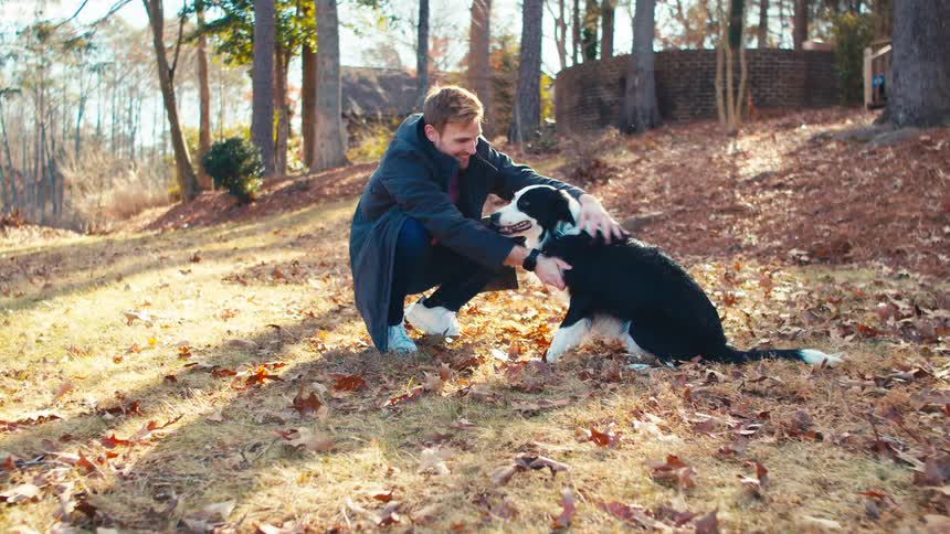 Man happily petting his dog outdoors in the wilderness on a sunny fall day