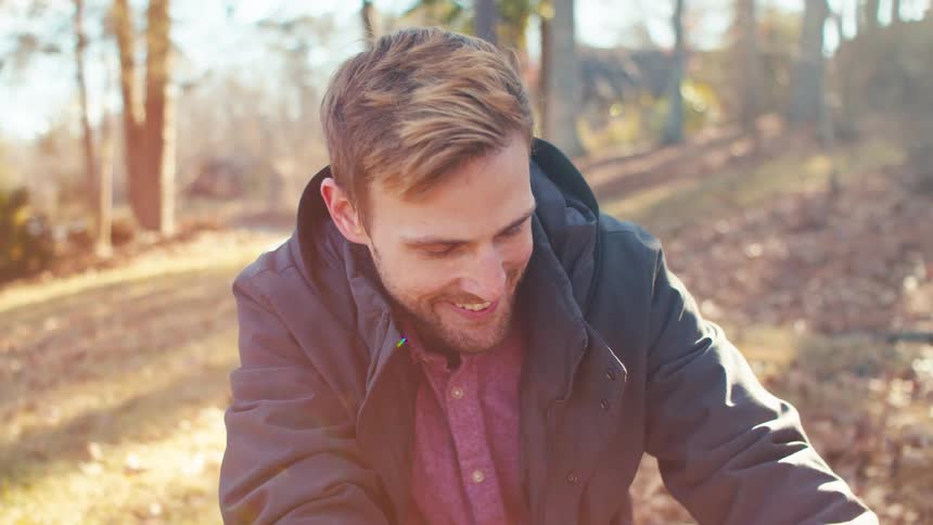 A man with light hair and a beard smiles down at a dog in a sunny outdoor setting
