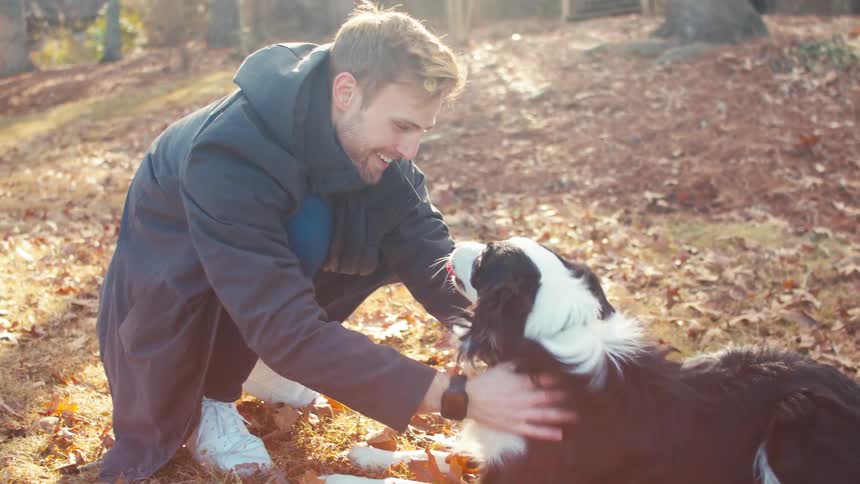 Man in blue coat happily petting his dog outdoors in the wilderness on a fall sunny day