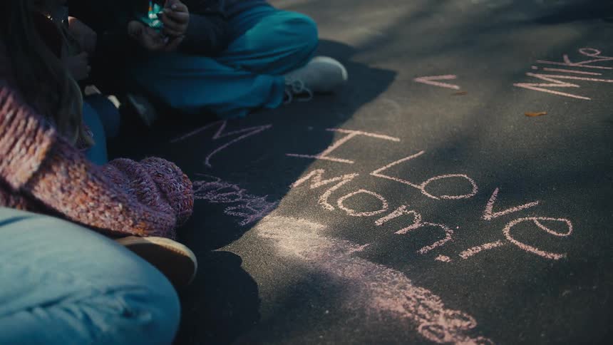 Two kids are sitting next to chalk writing on asphalt