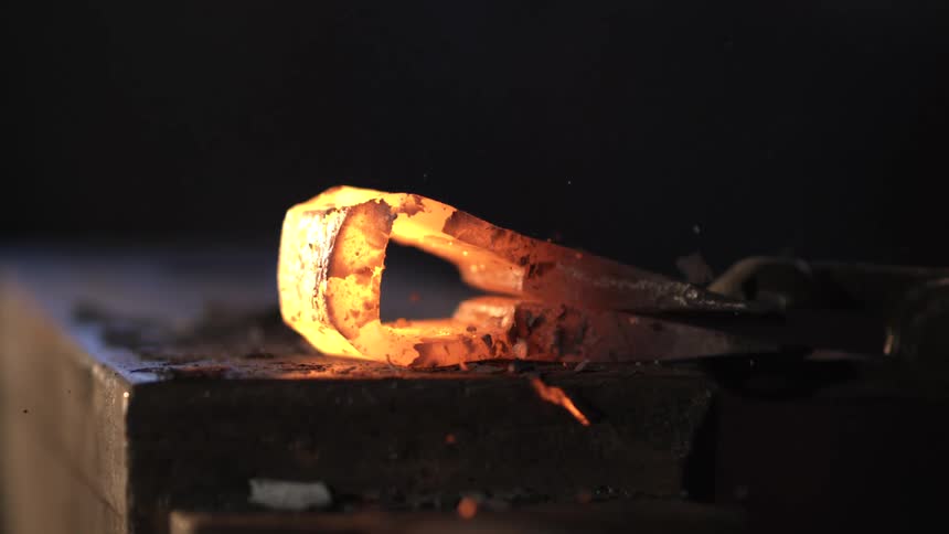 A hammer strikes a glowing hot piece of metal on an anvil sending sparks flying in a blacksmithing process