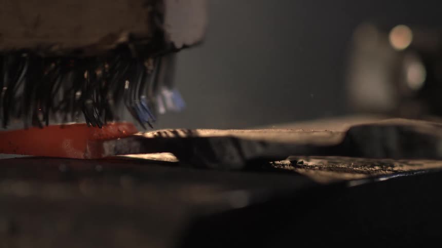 Sparks fly as the wire brush is used on the metal