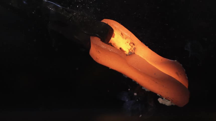 A worker turns an hot axe head with a pair of pliers