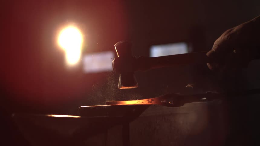 A man is hammering hot metal on an anvil