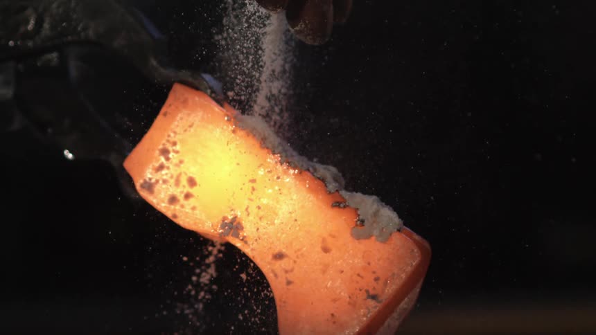 Heated piece being handled with tongs while a white substance is poured over it