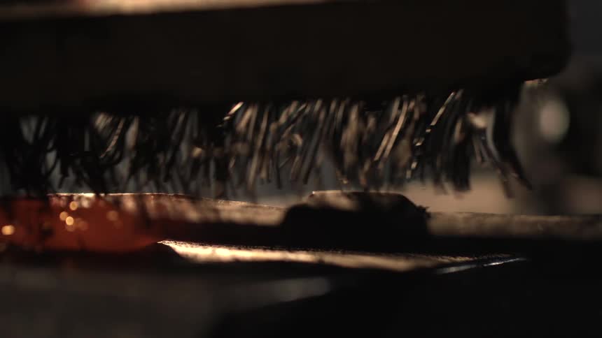 A wire brush is used to shave the hot metal