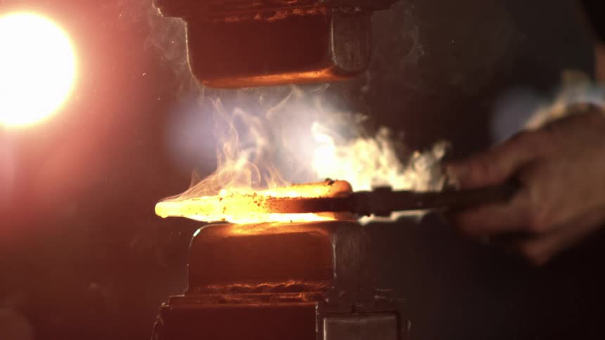 A man is using a hammer to work on red hot metal
