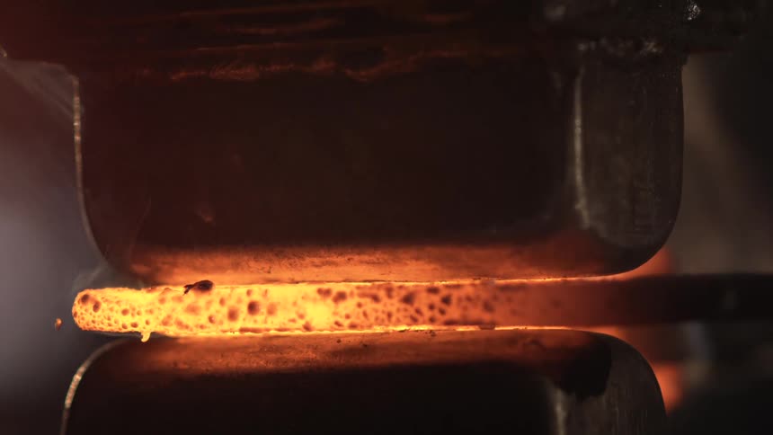 A piece of metal glowing orange hot under pressure is being forged
