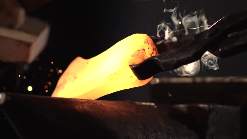 The blacksmith brushes the red hot metal on the anvil