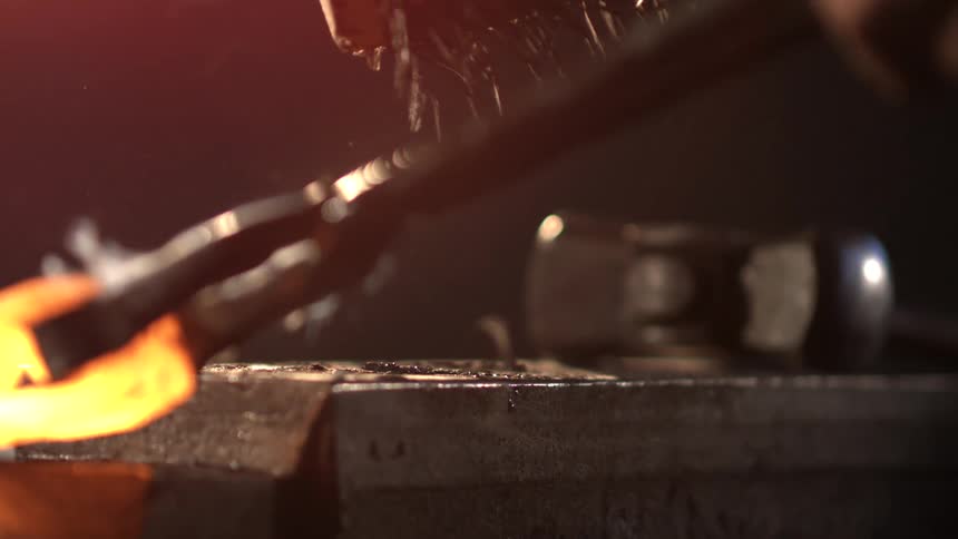 A blacksmith is working with a piece of hot metal on the anvil
