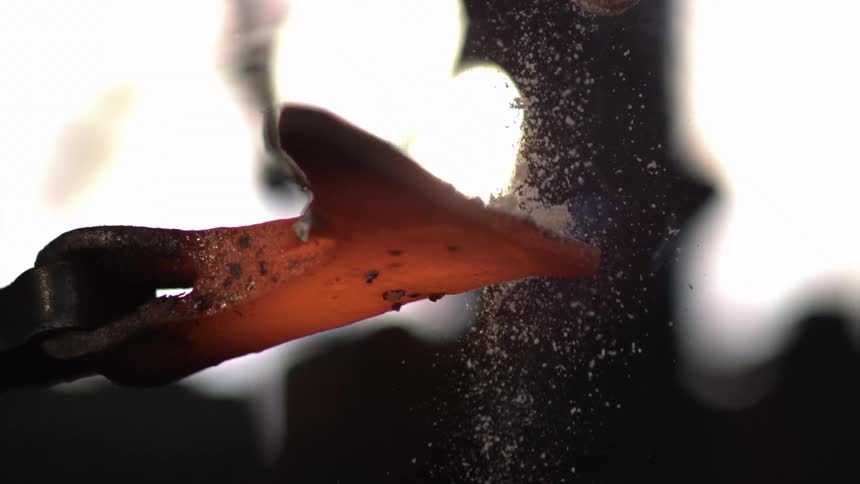 A blacksmith pours sand on the hot iron