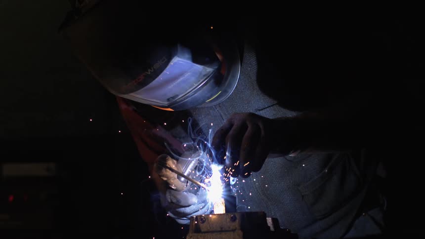 A worker wearing a mask and gloves is doing hot work on a piece of equipment