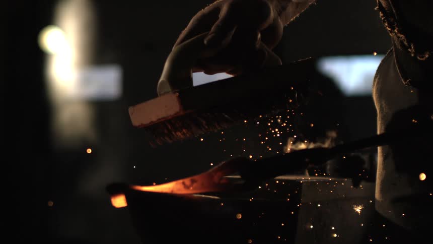 The blacksmith uses a wire brush on the hot metal