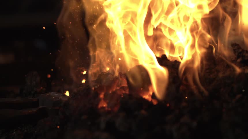 A closeup captures intense flames and glowing hot coals emitting a fiery redorange heat