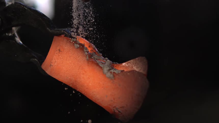 A footage of a blacksmith sprinkling a substance on a hot iron