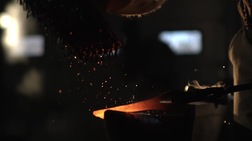 Blacksmith hits molten metal lying on an anvil with a metal brush