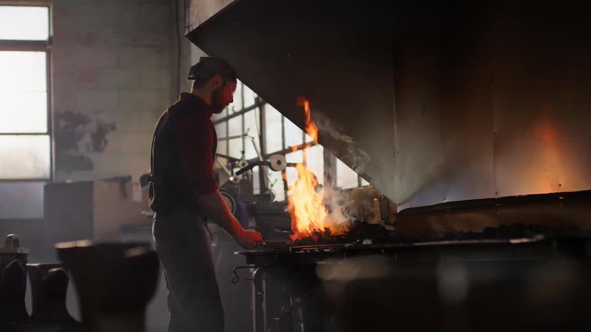 Man in a workshop forging in a fire with embers