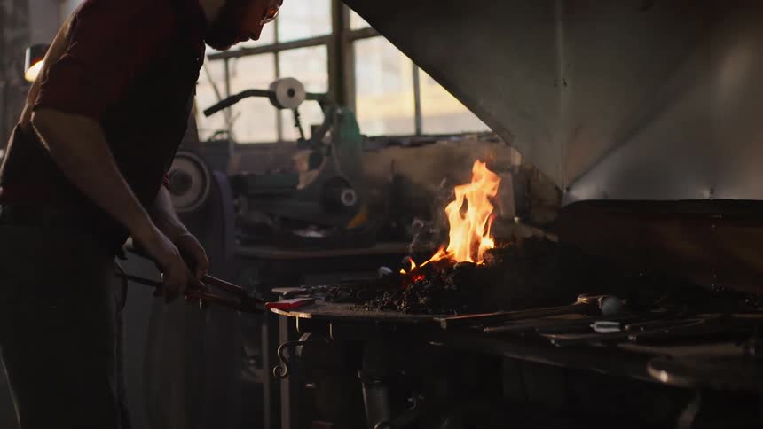 A man is working a metal piece in a forge
