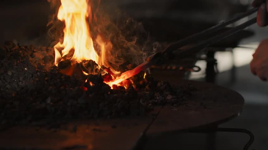 The blacksmith heats a piece of metal in the forge using tongs