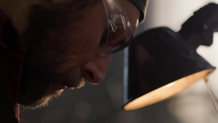 A man wearing safety glasses stands by a lamp looking down