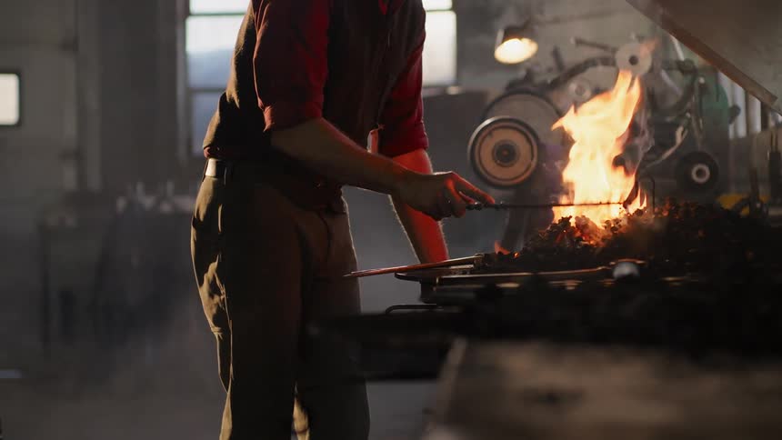 The blacksmith stirs the coal in the forge