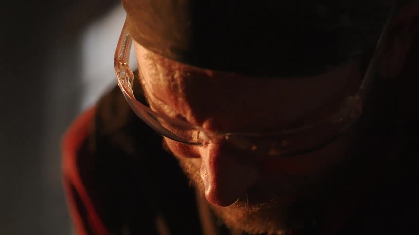 Man in work glasses beating something with a hammer