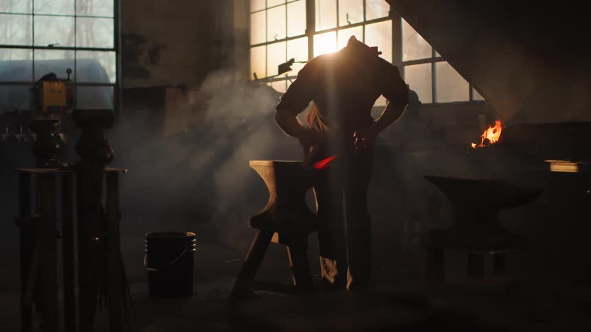 A man is hammering metal then moves to put it in the fire