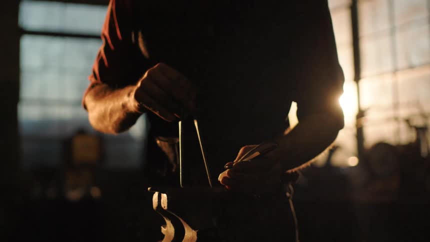 Man holds metal parts while working at a workbench illuminated by soft light coming through the window