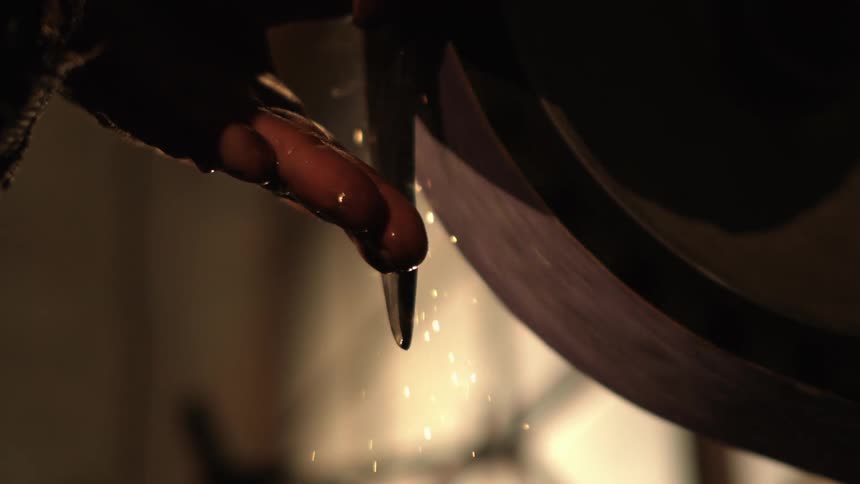 A person holds a blade to a grinding stone