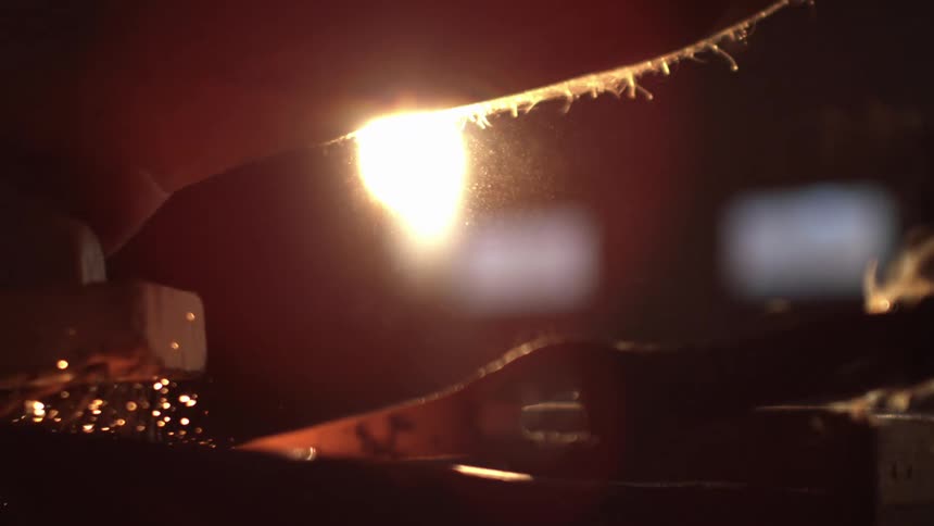 A tool with fine wire like bristles is used to smooth out a hot glowing orange object creating sparks as it moves