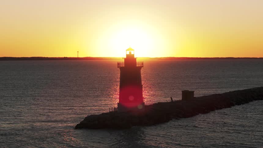 A lighthouse standing at the end of a path with a calm ocean and the sun setting
